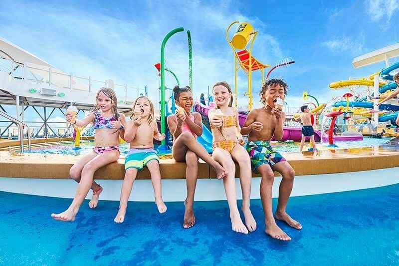 Kids sitting at a colorful water park, smiling with legs dangling by a splash pool