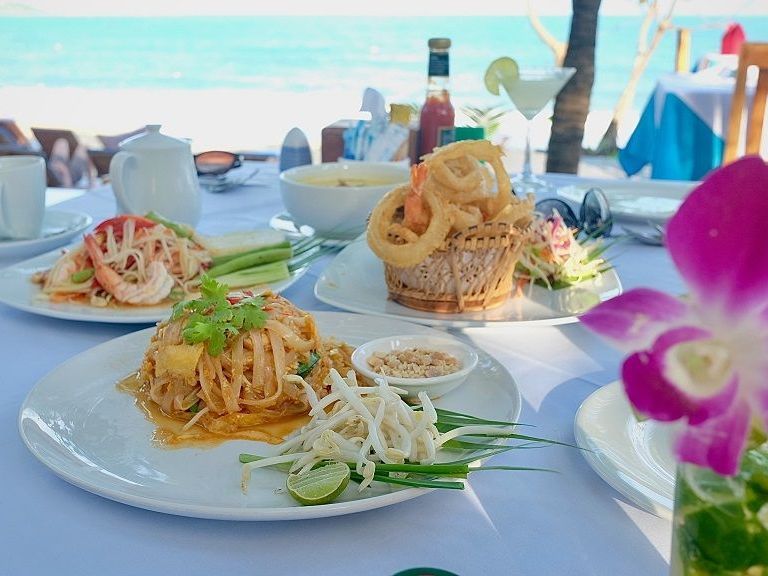Plated pasta dishes on a beachside table with ocean view and a purple orchid in the foreground