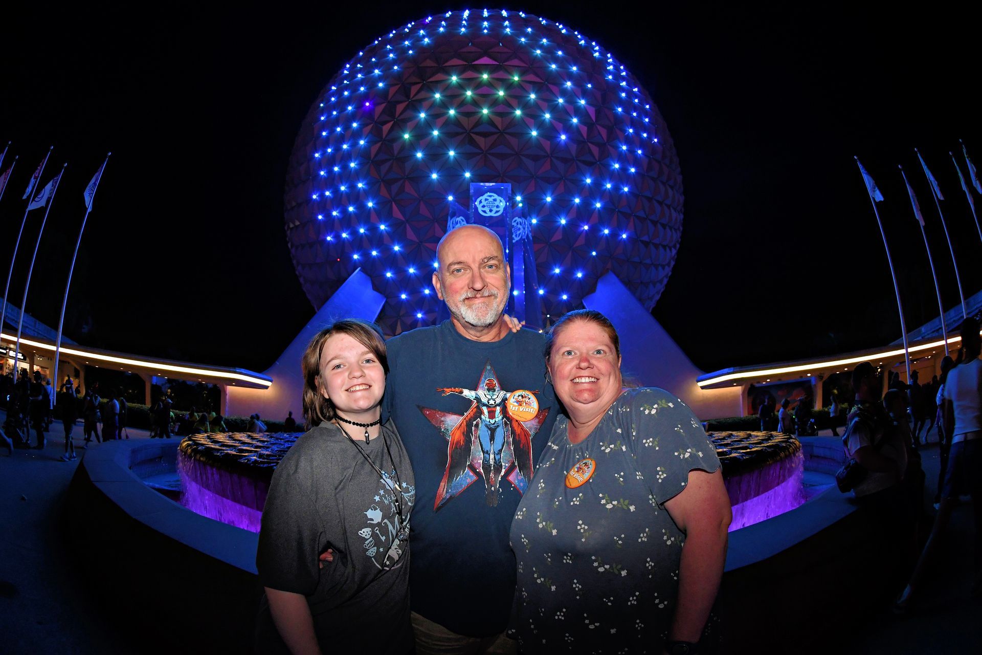 Three people posing at night before a glowing blue spherical light display.