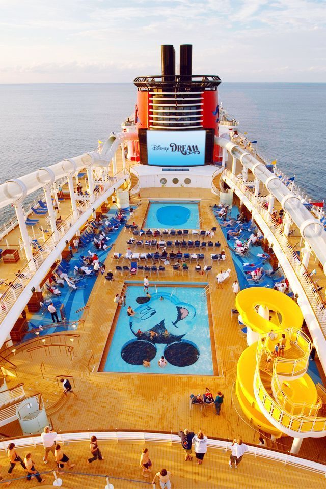 Cruise ship pool deck with swimmers, blue pools, and bright yellow water slides at sea