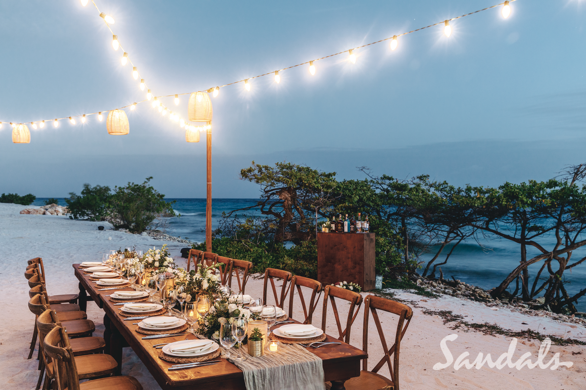 Elegant seaside dining table with string lights at sunset, overlooking the ocean and rocks.