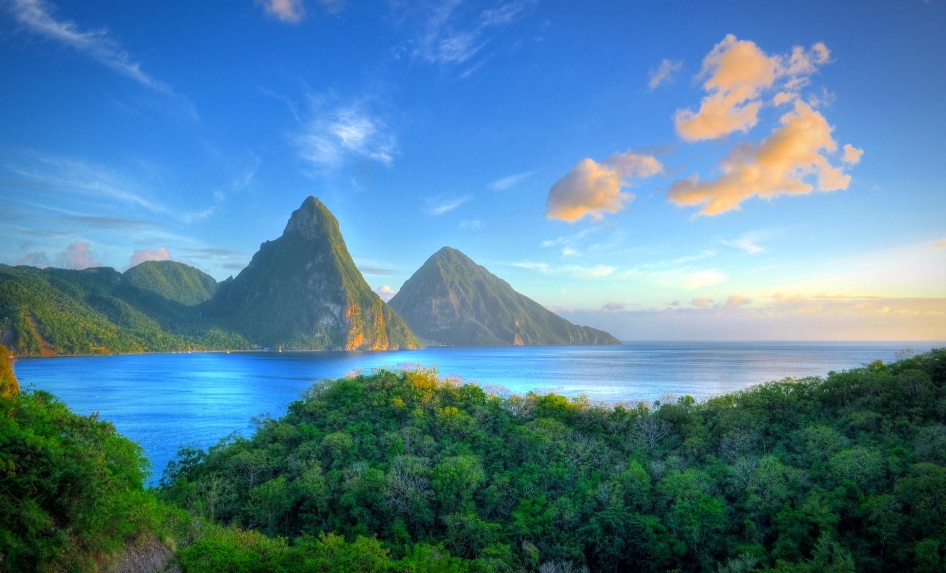 Tropical bay with blue water, lush green mountains, and a bright sky at sunrise