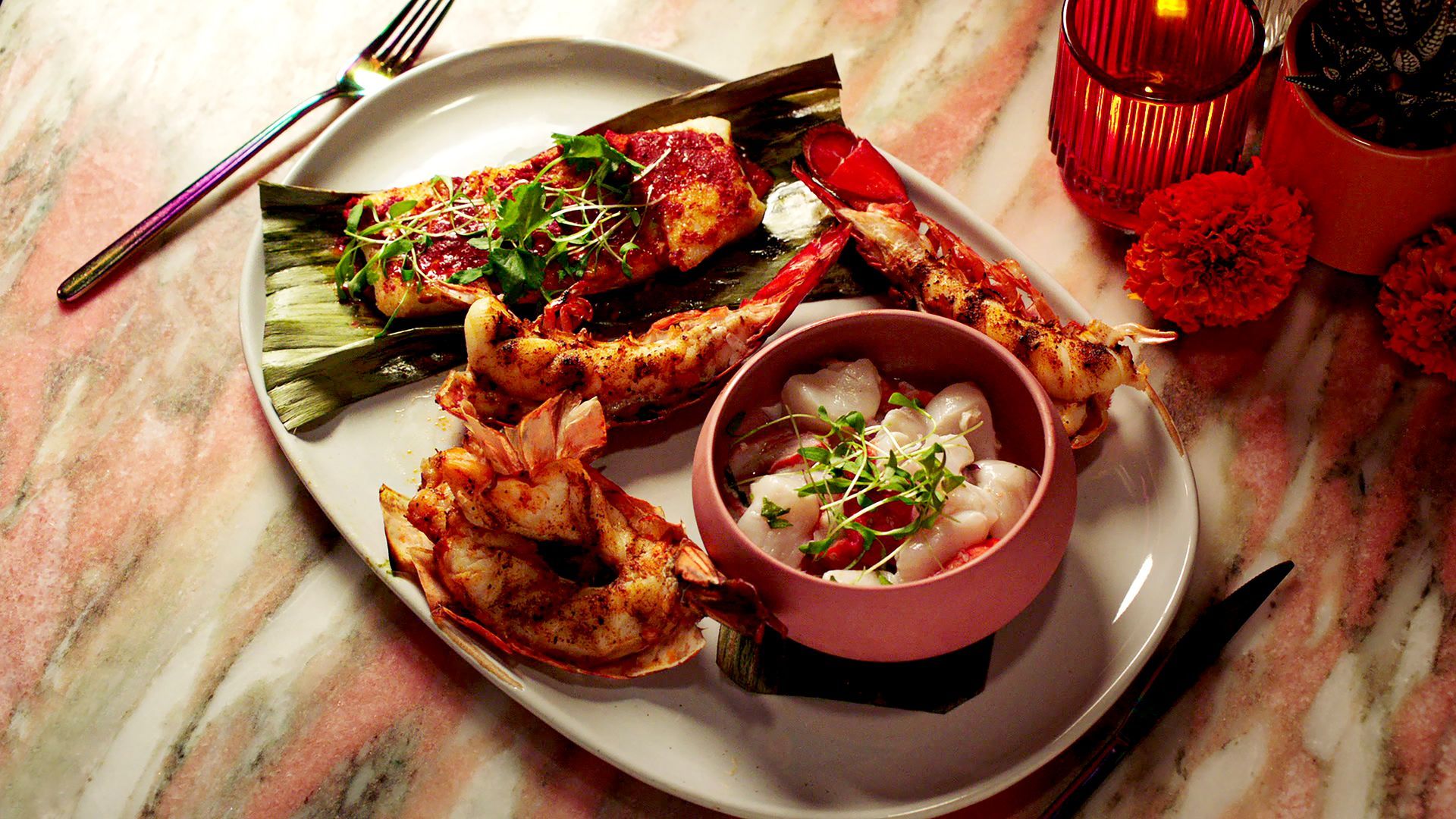 Plated roasted chicken with greens and sauce on a table, beside a red candle and utensils