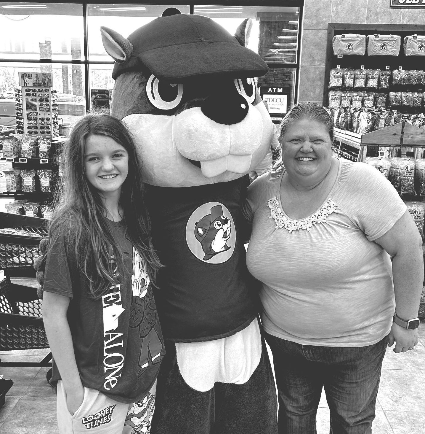 Two smiling shoppers pose with a large mascot in a store aisle.