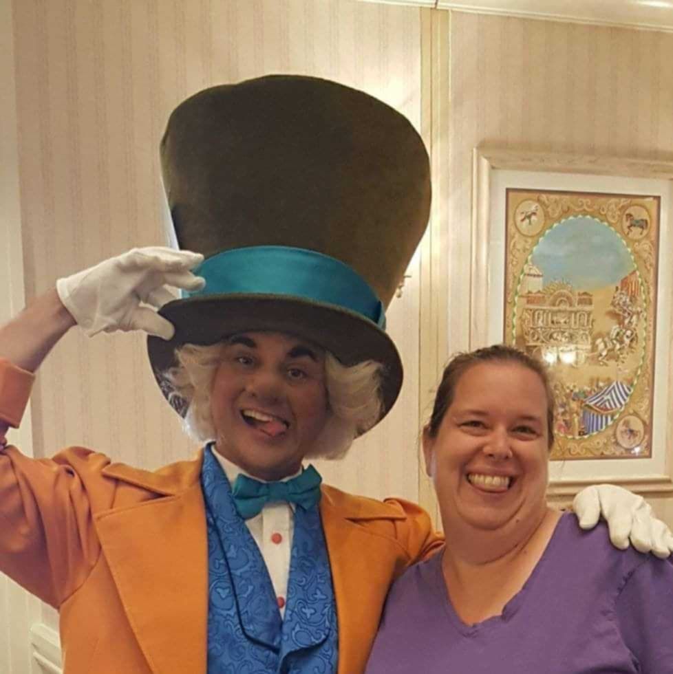 Person in a tall hat and blue suit poses with a smiling woman indoors.