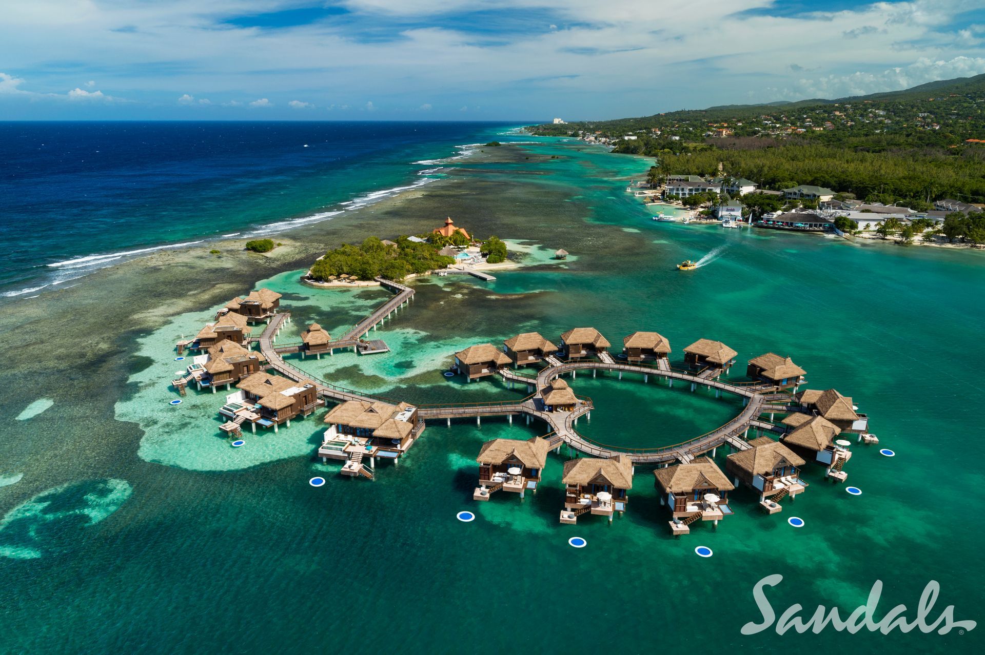 Aerial view of turquoise resort lagoon with overwater bungalows and a sandy island coastline