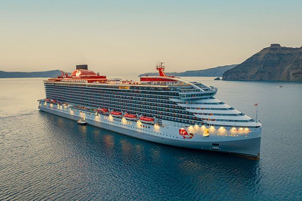 Large white cruise ship at sea near a rocky coastal island at sunset