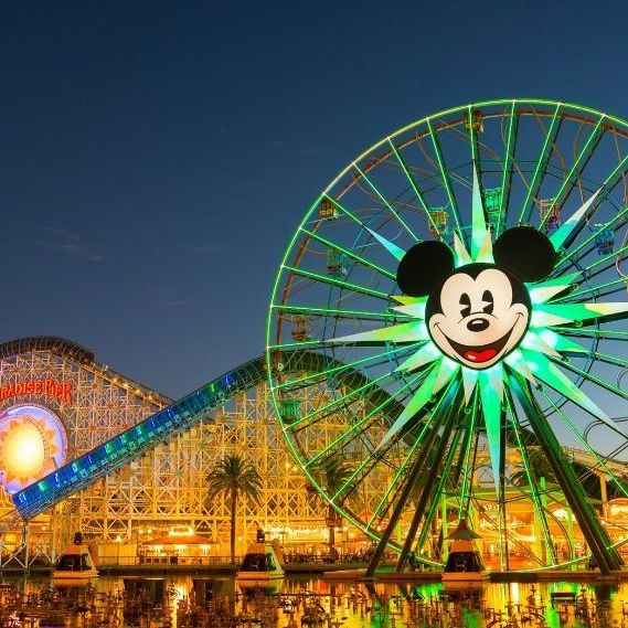 Mickey Mouse Ferris wheel glowing green at Disneyland at night, with a lit roller coaster in the background