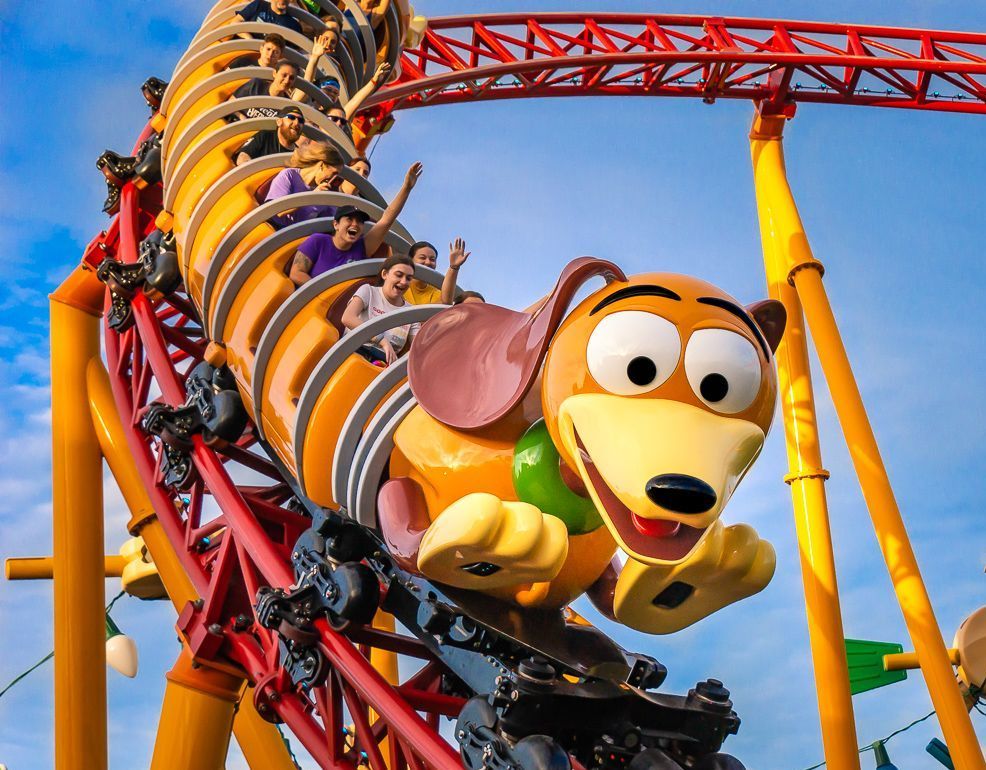 Snoopy-themed roller coaster with smiling riders on a red track against a blue sky
