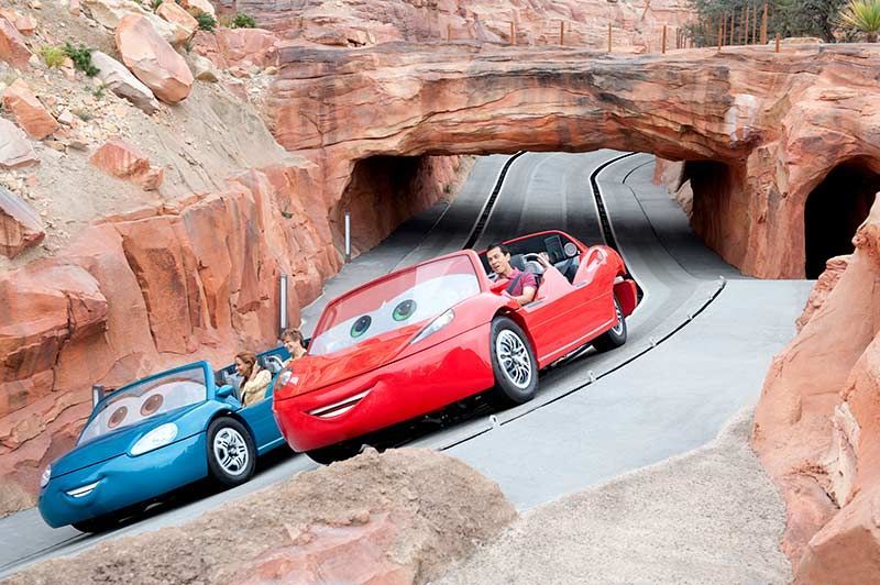 Two red sports cars and a blue car driving through a rocky tunnel in a desert-themed ride