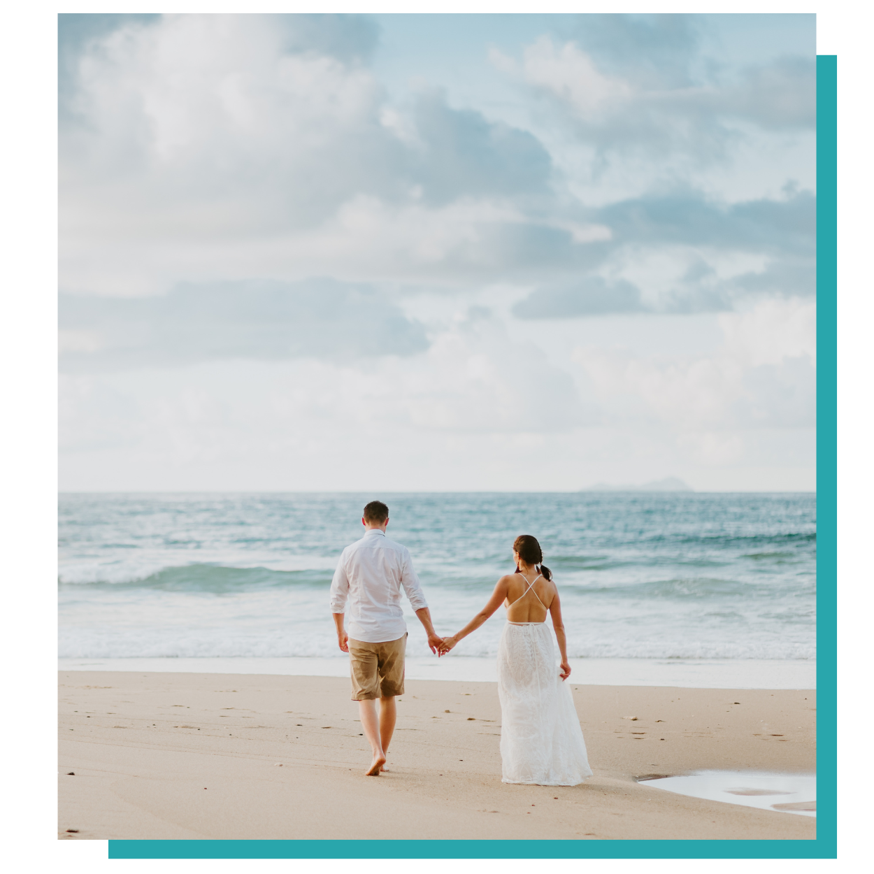 Couple holding hands and walking barefoot on a beach toward the ocean under cloudy skies
