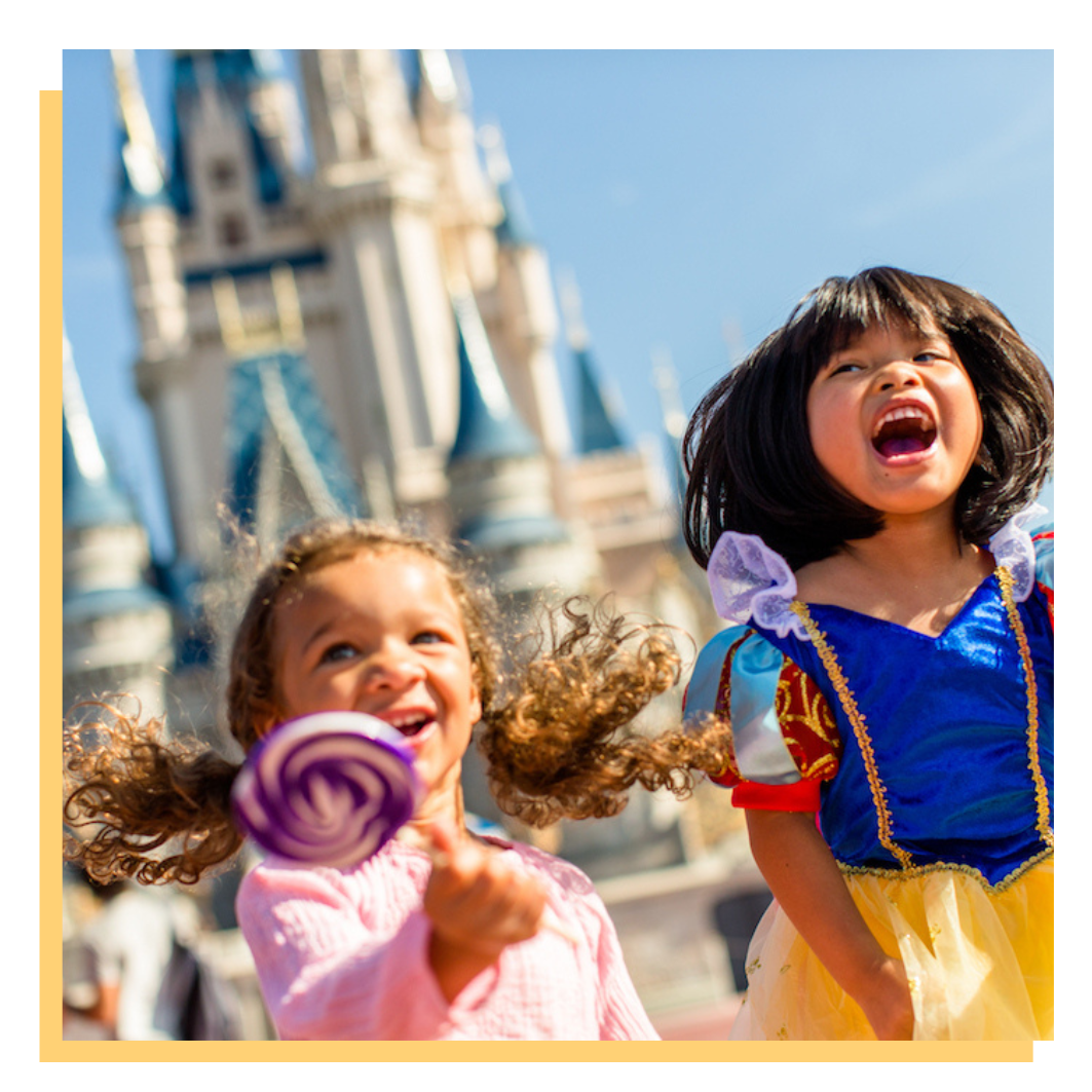 Two children smiling in front of a castle, one holding a pink lollipop