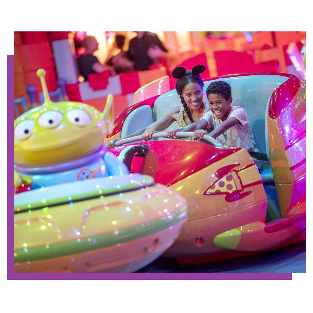 Two people riding a colorful spinning amusement ride, smiling in a bright neon-lit carnival setting