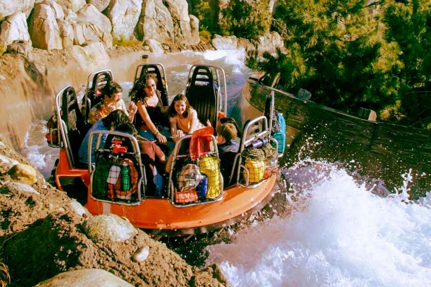 Raft with riders splashing through rapids beside rocky cliffs and greenery
