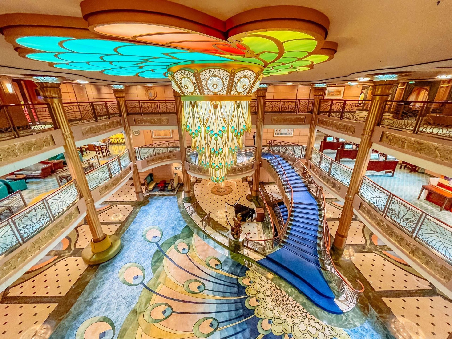 Grand atrium with a blue staircase, decorative columns, balconies, and a colorful ceiling mural