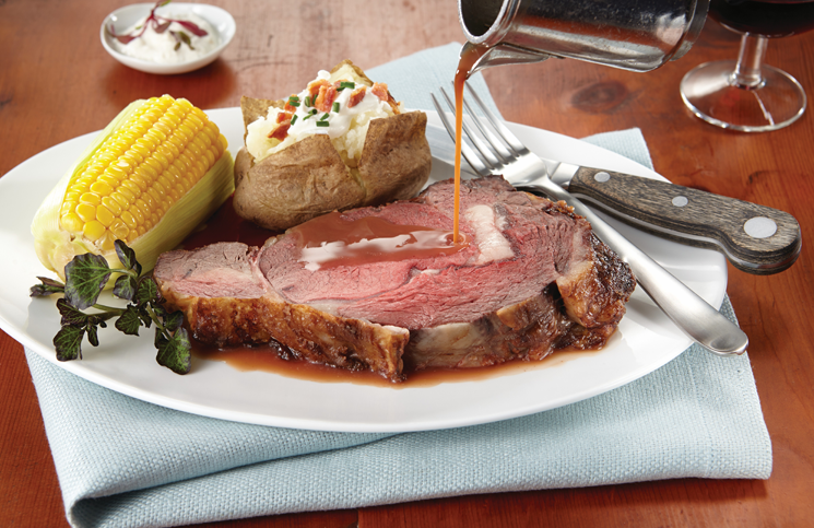 Roast beef dinner with corn, baked potato, and gravy being poured onto the plate