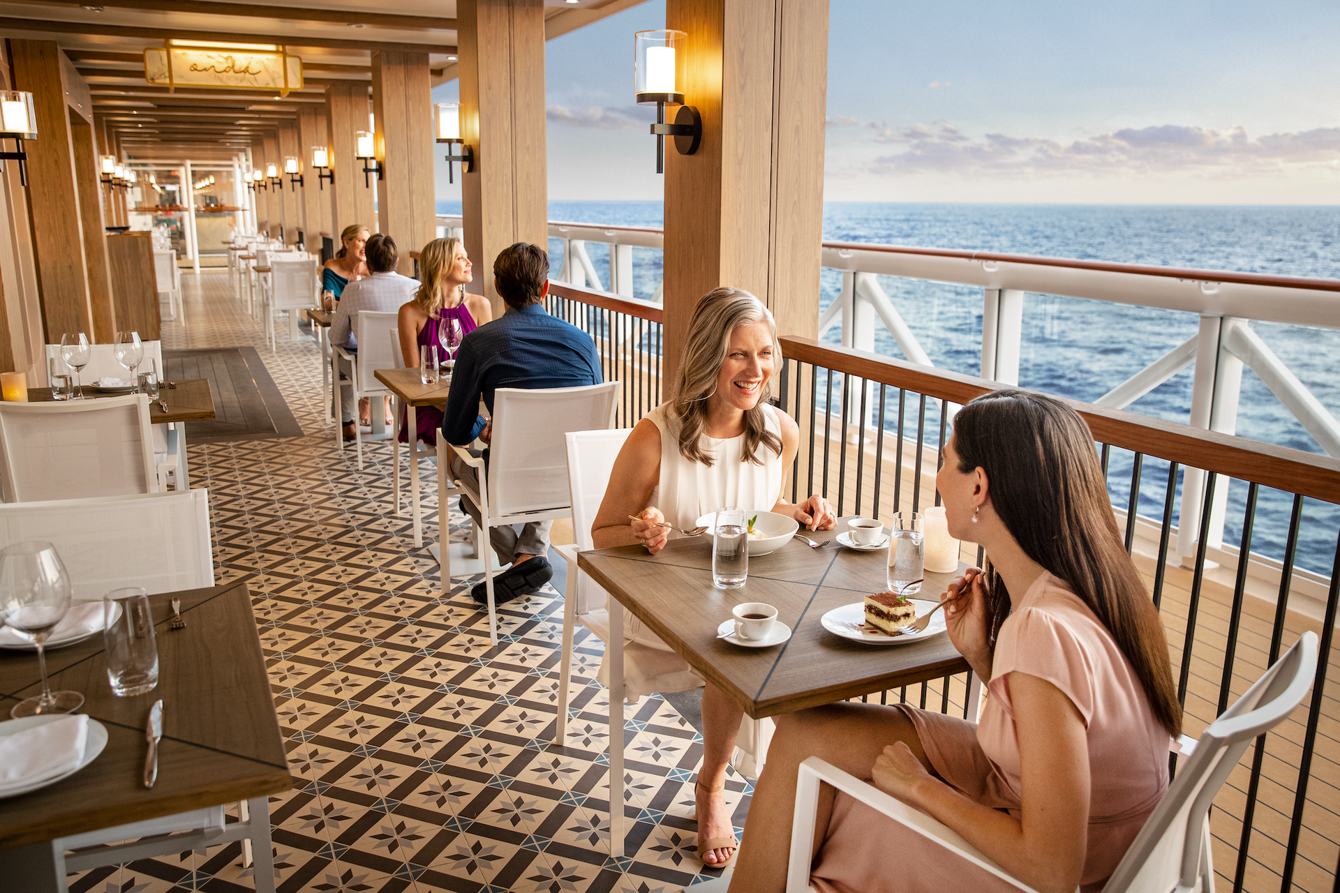 Open-air seaside restaurant with two diners at a table overlooking the ocean at sunset