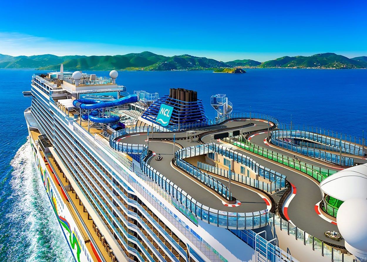 Cruise ship deck with pools and waterslides overlooking a bright blue ocean and distant green islands