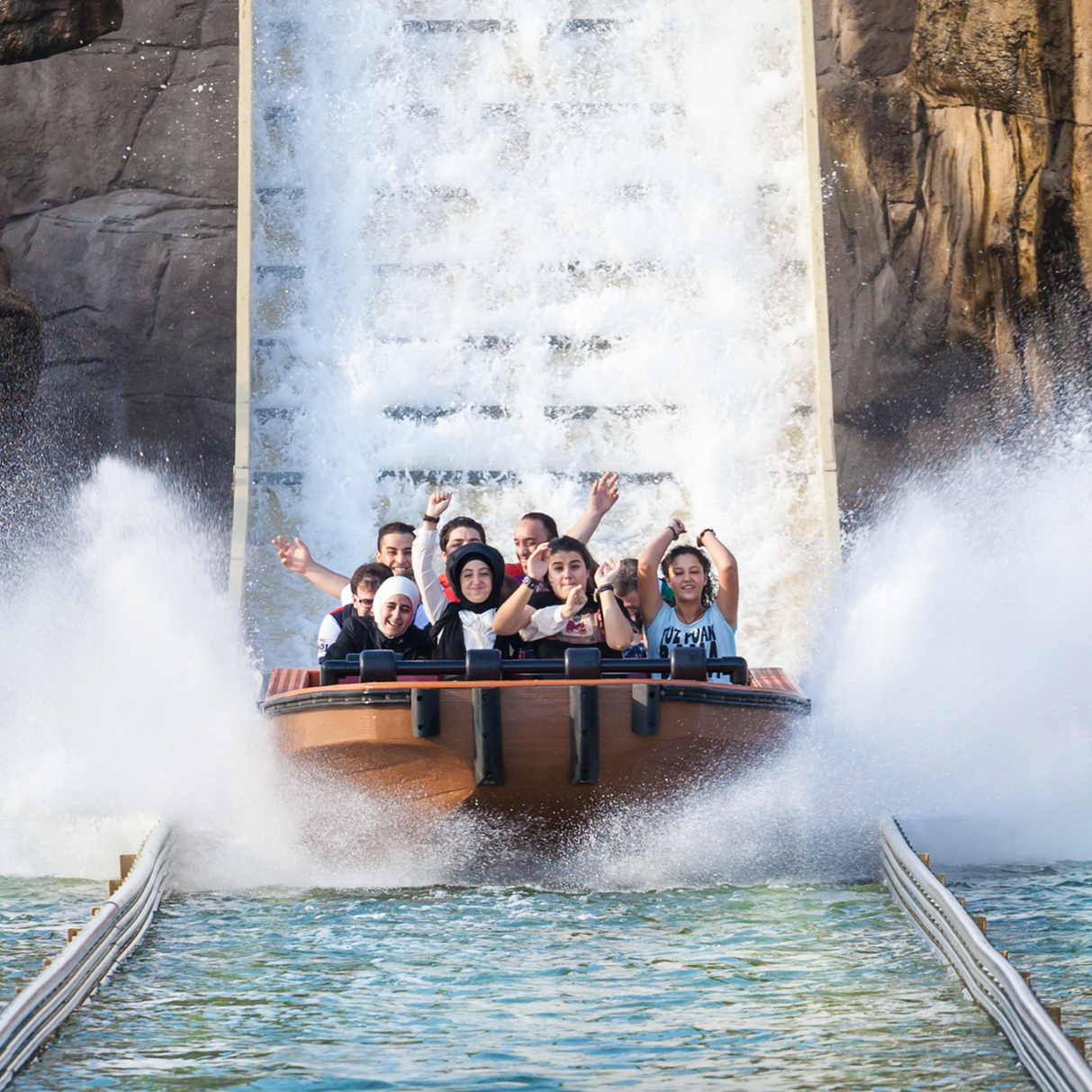 Thrill ride boat plunging down a waterfall with riders cheering and splashing water