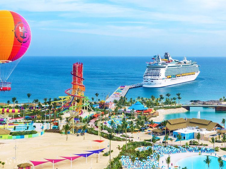 Waterpark by the sea with cruise ship, colorful hot air balloon, and bright pools under a blue sky