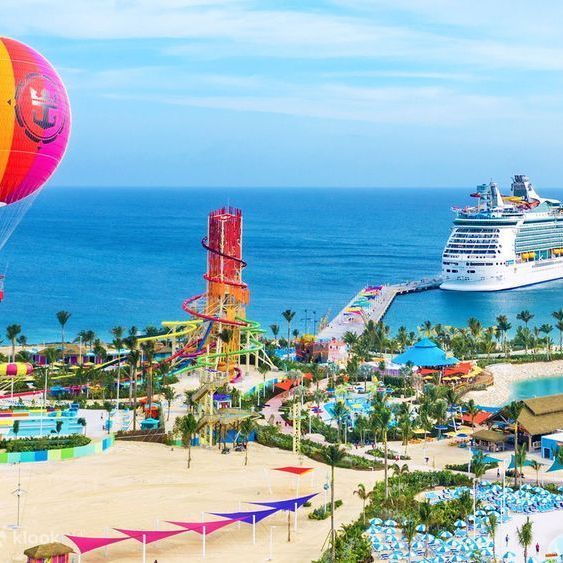 Cruise ship docked by a tropical beach resort with a hot air balloon and water park tower