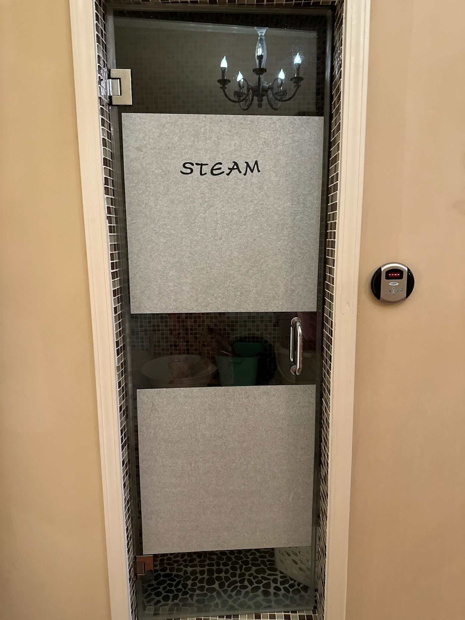 A glass door to a steam room with privacy-frosted panels, marked with the word 