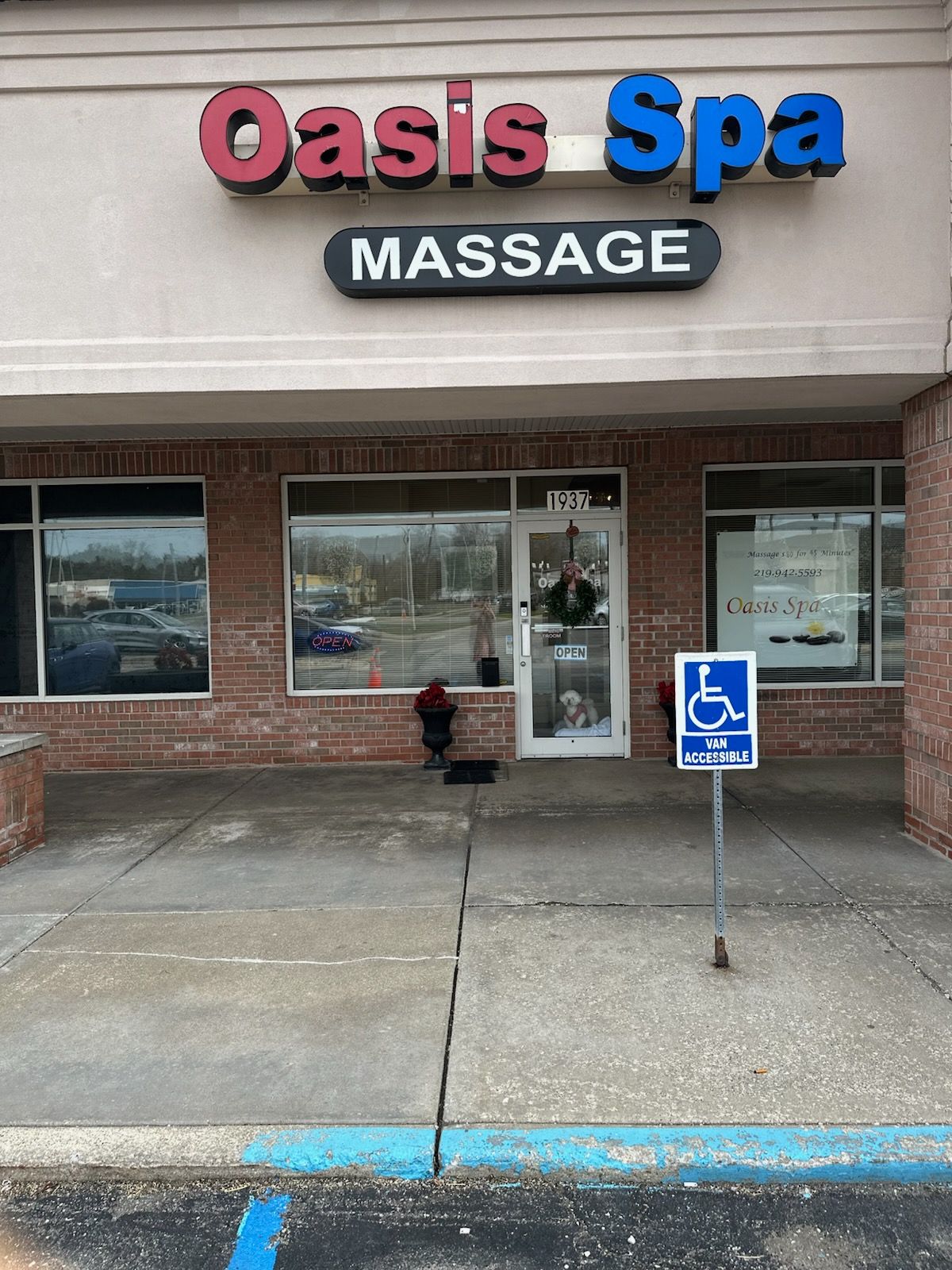 Front view of the Oasis Spa Massage storefront with a handicap parking sign on the sidewalk in front of the glass door.
