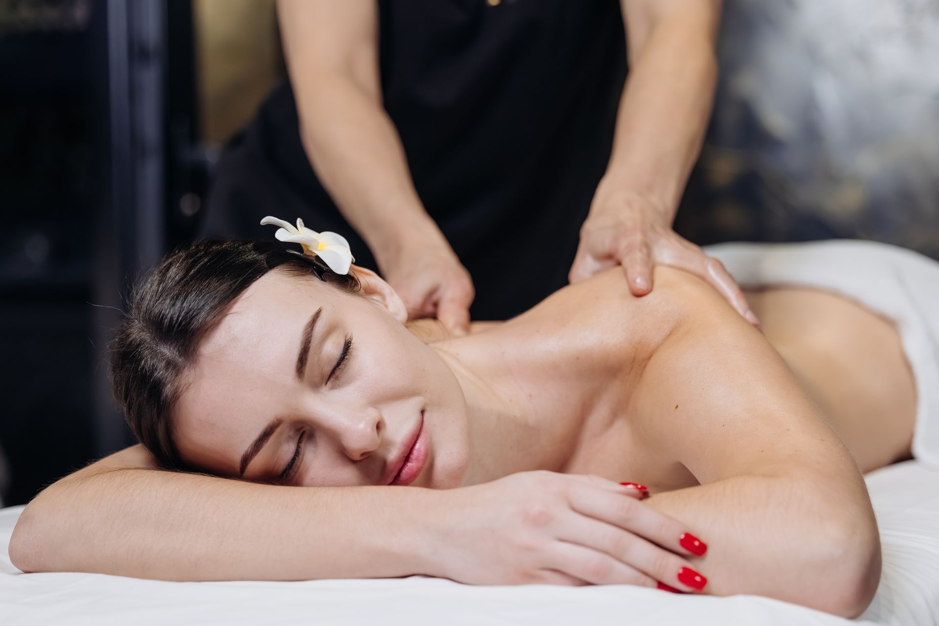 A person with a flower in their hair lies relaxed on a spa table while receiving a professional back massage.