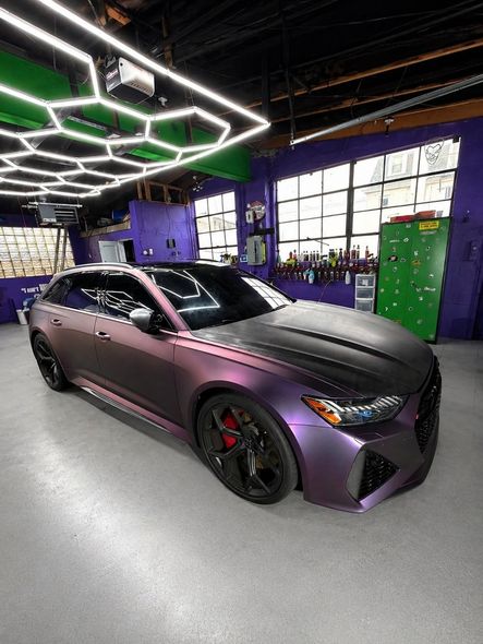 Purple sports car in a neon-lit garage with black wheels and geometric ceiling lights.