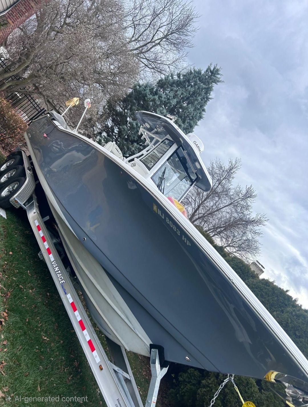 Large gray boat on a trailer, tilted in a yard beside trees under a cloudy sky