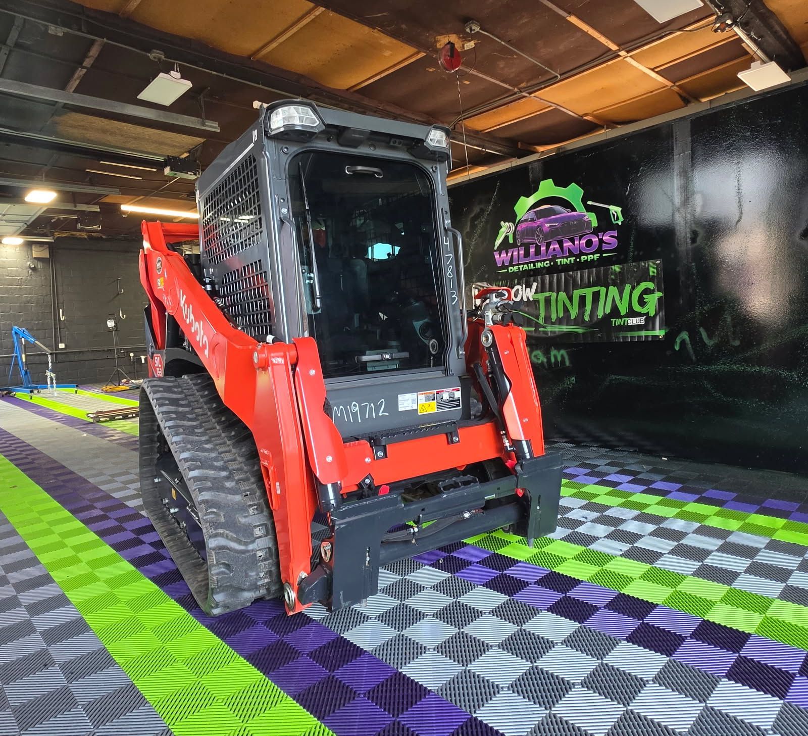 Red skid-steer loader inside a detail shop with purple, green, and checkered floor mats.