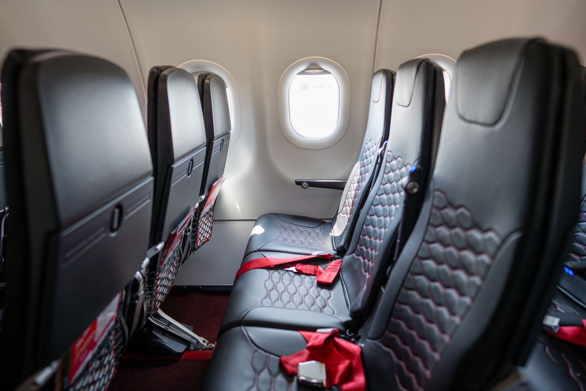 Small airplane cabin with black leather seats and a red seat belt, viewed from the aisle.