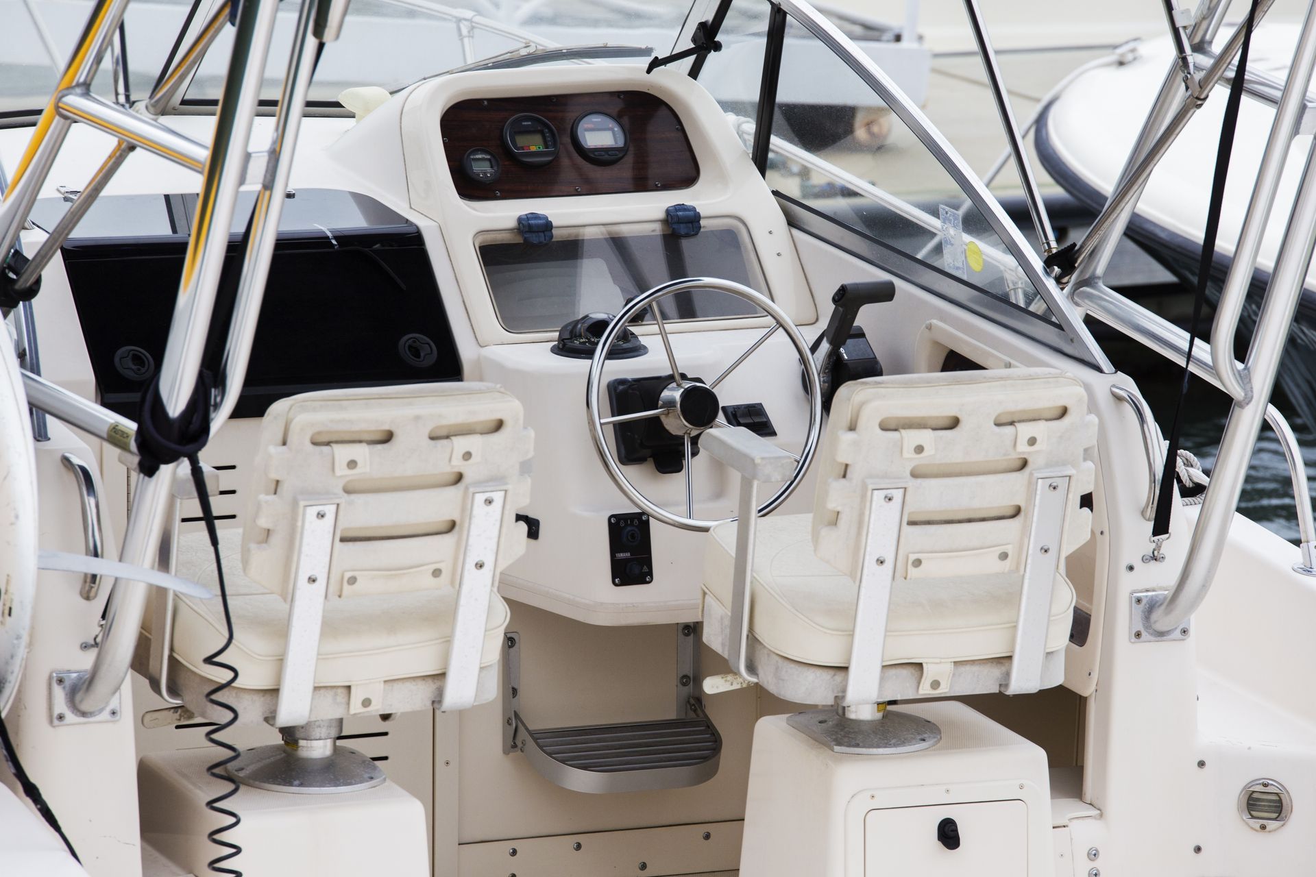 Boat cockpit with twin white seats, steering wheel, dashboard, and metal railings.