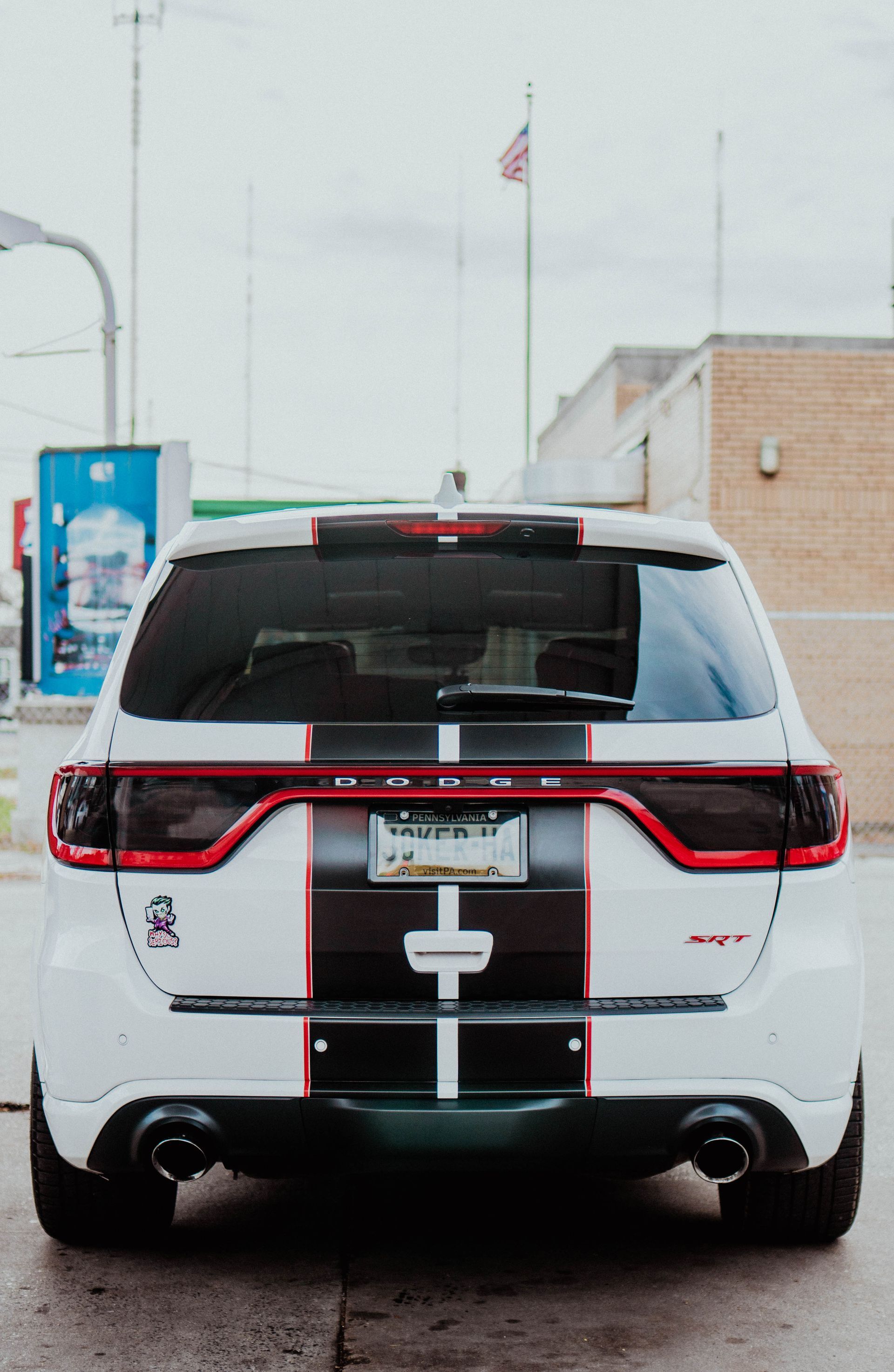 Rear view of a white SUV with red taillight strip parked outside a building.