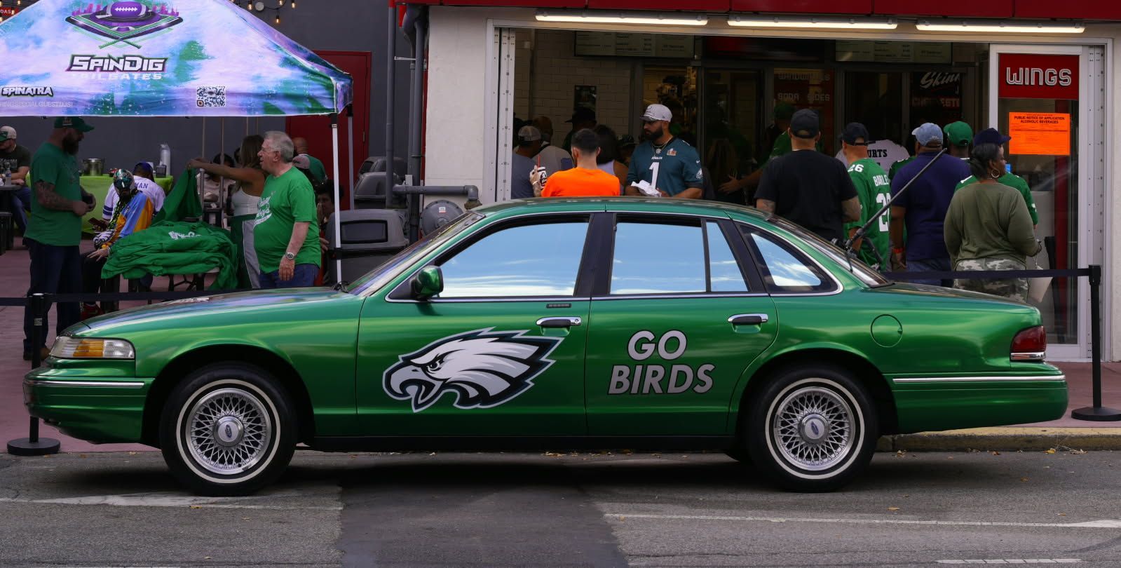 Green sedan with Eagles logo and “GO BIRDS” text parked on a street outside a busy shop.