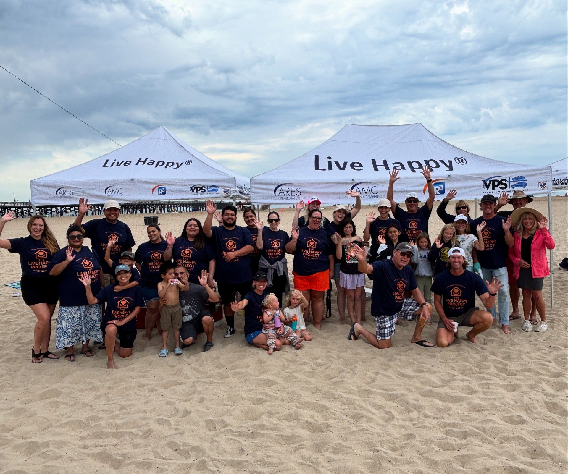 Live Happy Project team members under two white tents on the beach at Seal Beach 