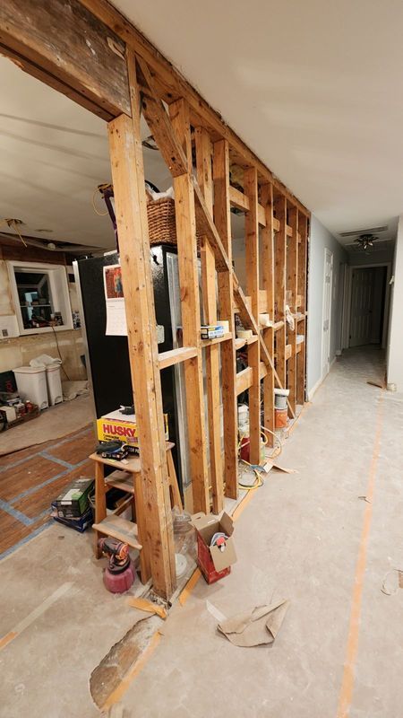 Exposed wooden wall studs in a hallway during home renovation, with debris on the floor.