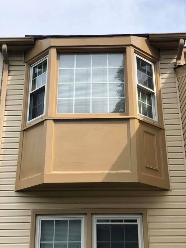 Tan bay window on a beige house exterior with white-framed windows