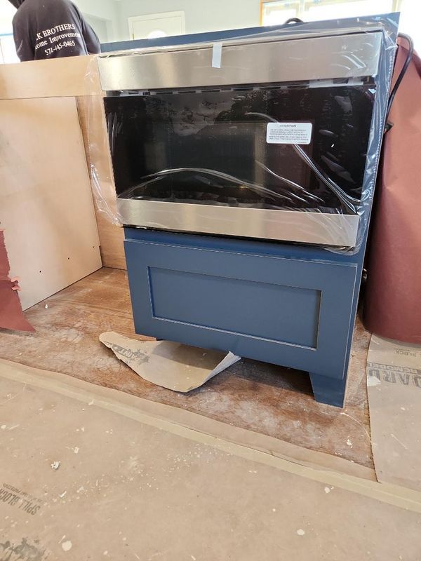 Blue oven or stove unit in a workshop, partially wrapped in plastic and cardboard.