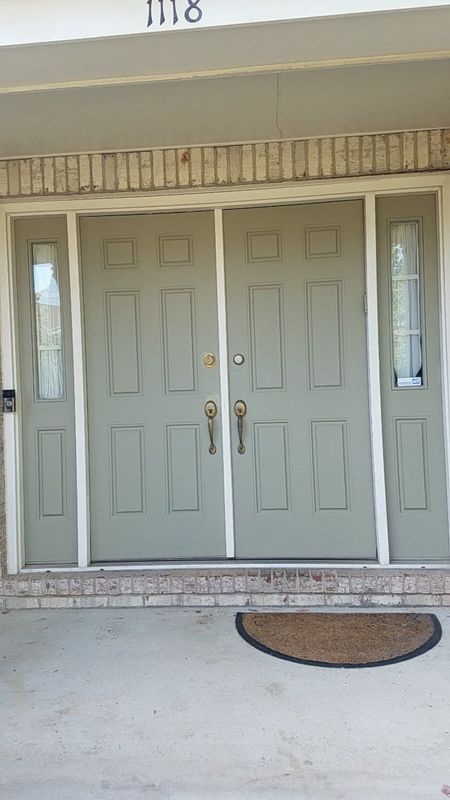 Front entrance with beige double doors, sidelights, and a doormat on a covered porch.
