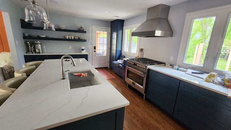 Modern kitchen with marble island, black cabinets, stainless range, open shelves, and bright windows