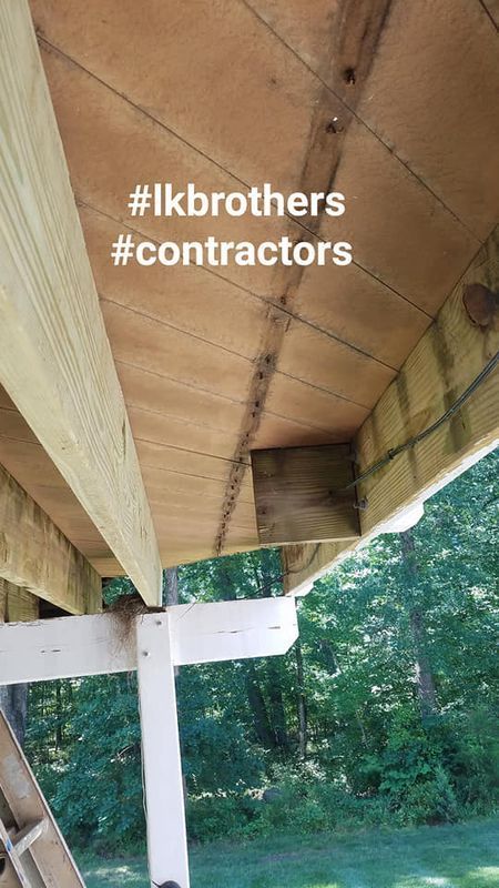 Under-deck view of a wooden porch with white posts and green yard beyond, overlaid with “#lkbrothers #contractors”