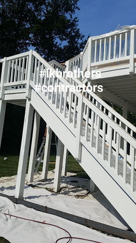 White outdoor staircase with railings and deck under a blue sky, with a tree in the background.