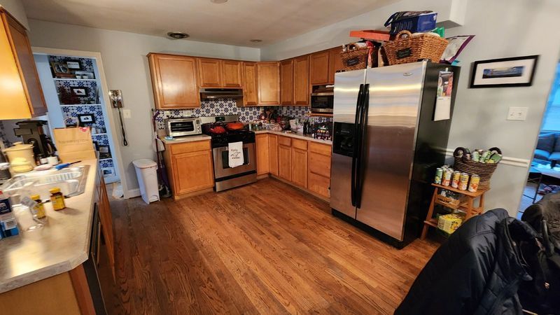 Modern kitchen with wooden cabinets, stainless steel fridge, gas stove, and hardwood floors