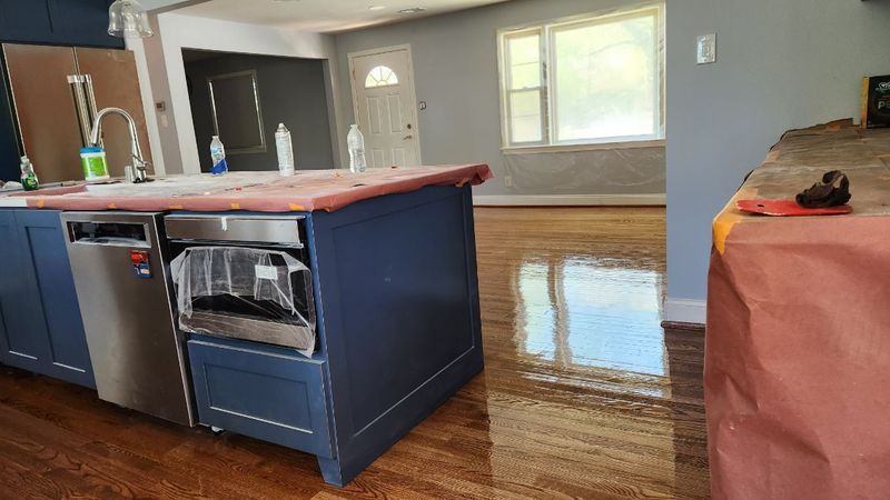 Modern kitchen with blue island, dark hardwood floors, and sunlight reflecting from windows