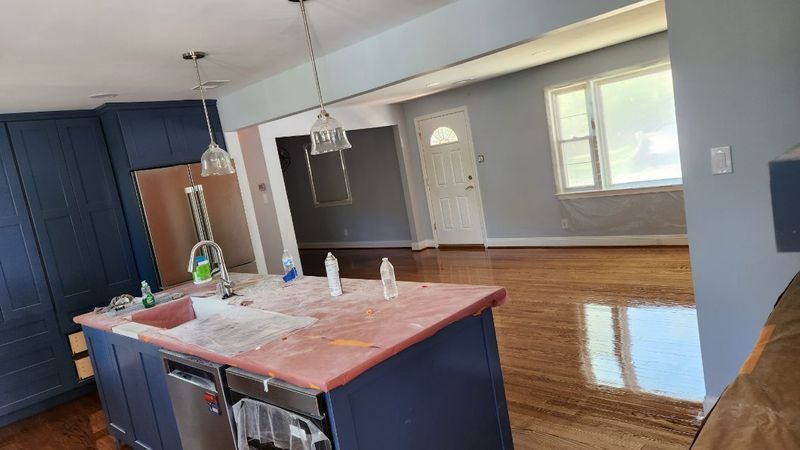 Kitchen with dark blue island, red countertop, and open view into a bright hardwood living area.