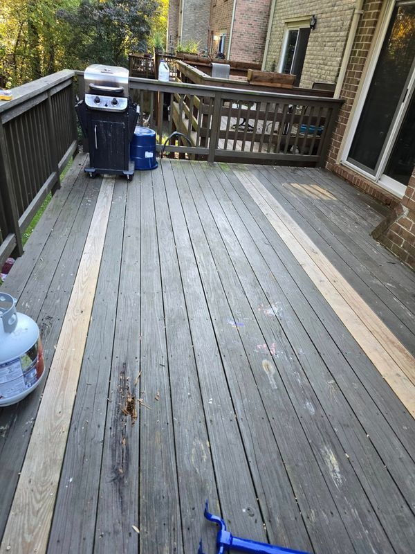 Wooden deck with railing, grill, and blue propane tank beside a brick house and sliding door