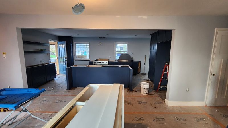 Renovation site with exposed flooring, a kitchen island, cabinets, and construction materials scattered around