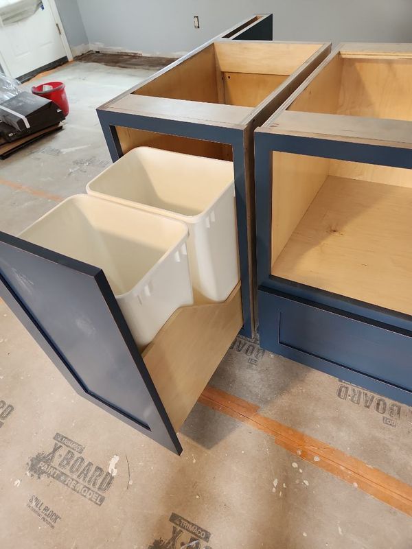 Open cabinet with white bins under a wood-and-black counter in an unfinished room.