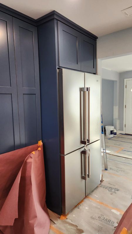 Kitchen with dark navy cabinets, stainless steel refrigerator, and unfinished floor under renovation
